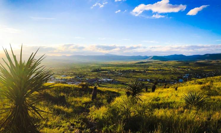 View of Alpine, Texas, from atop a nearby hill. The grasses are lush and green and the sky is a vibrant blue.