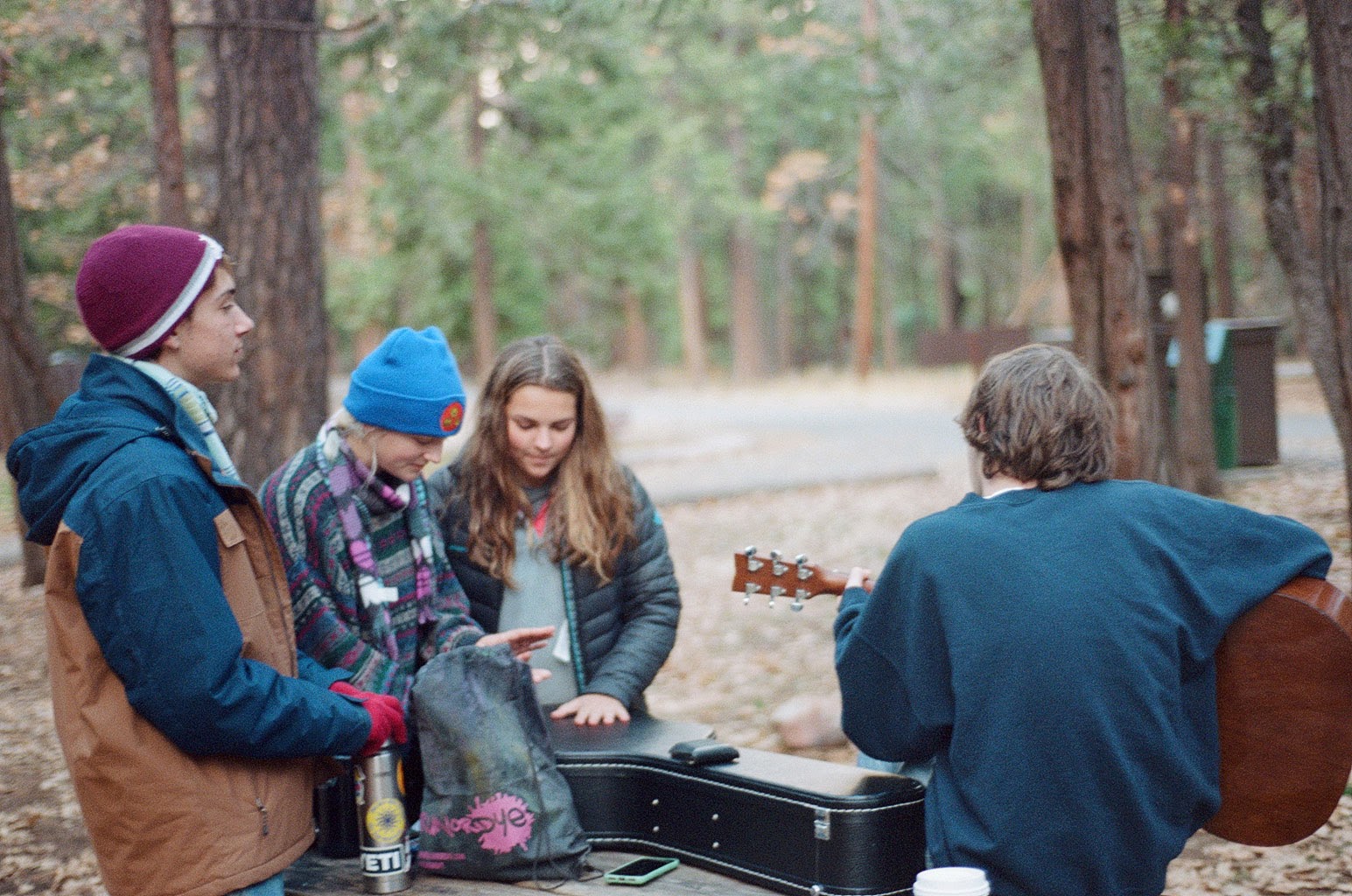 The group sitting in the forest and playing guitar