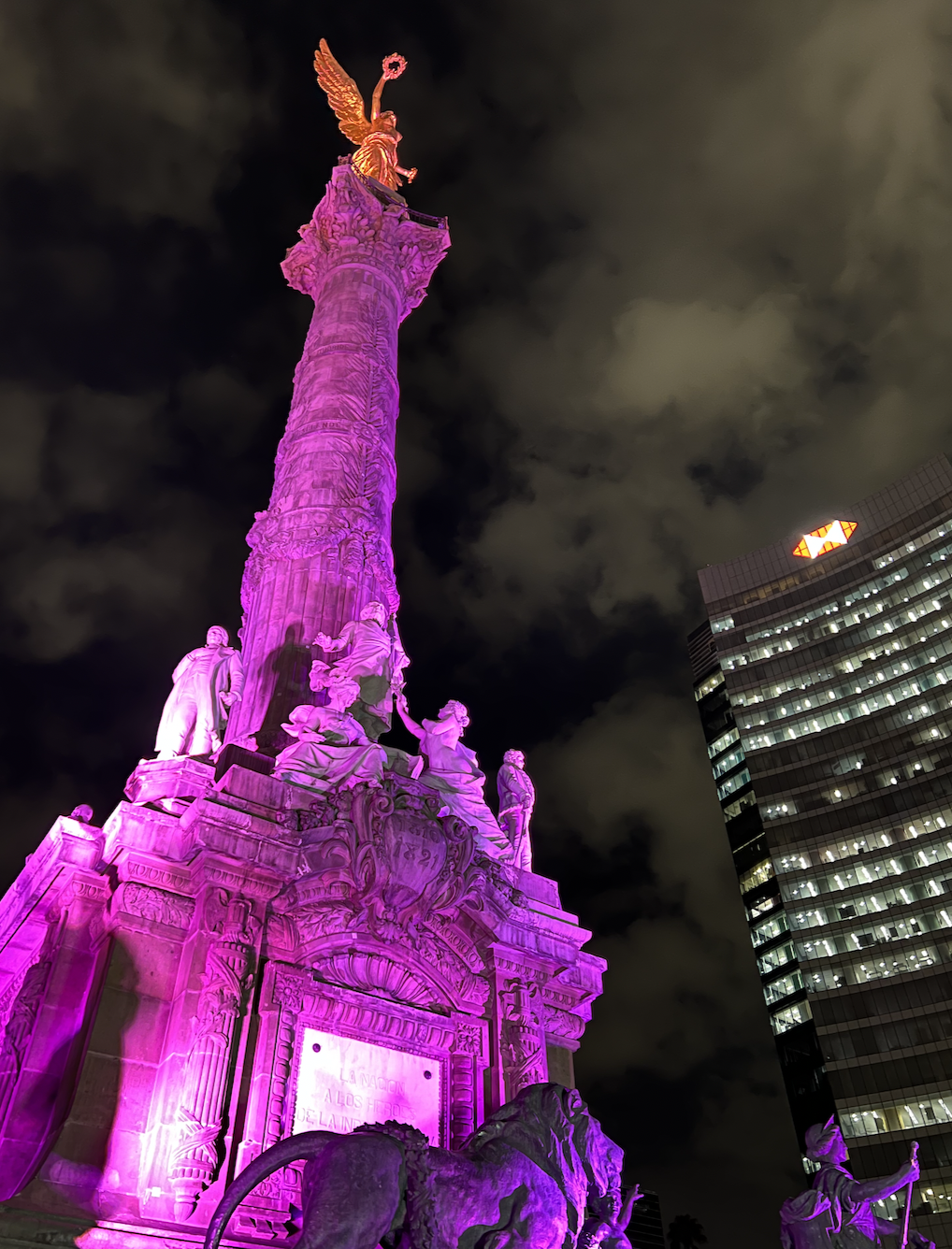 angel of independence at night with a pink light shining on it. 