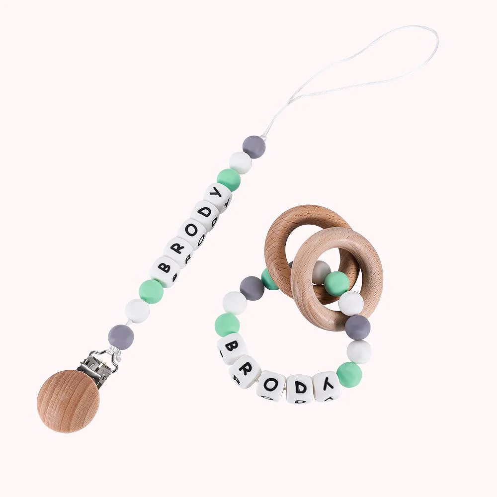 Attache sucette avec bout en bois et ficelle décorée de perles avec personnalisation par un prénom. 2 anneaux de dentition reliés entre eux par des perles avec personnalisation par un prénom. 
