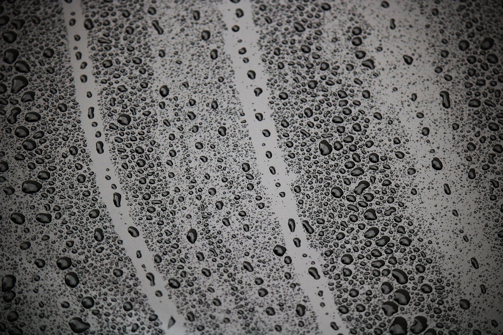 Droplets of water that appear to be evaporation or condensation are gathered and sliding down a smooth surface.