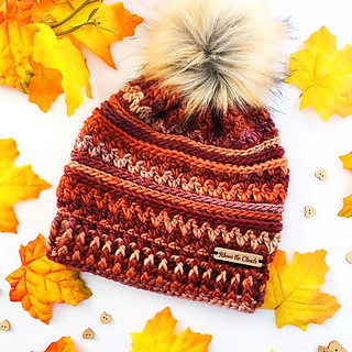 fall colored crochet beanie with faux fur pom pom lying flat on white background with leaves surrounding