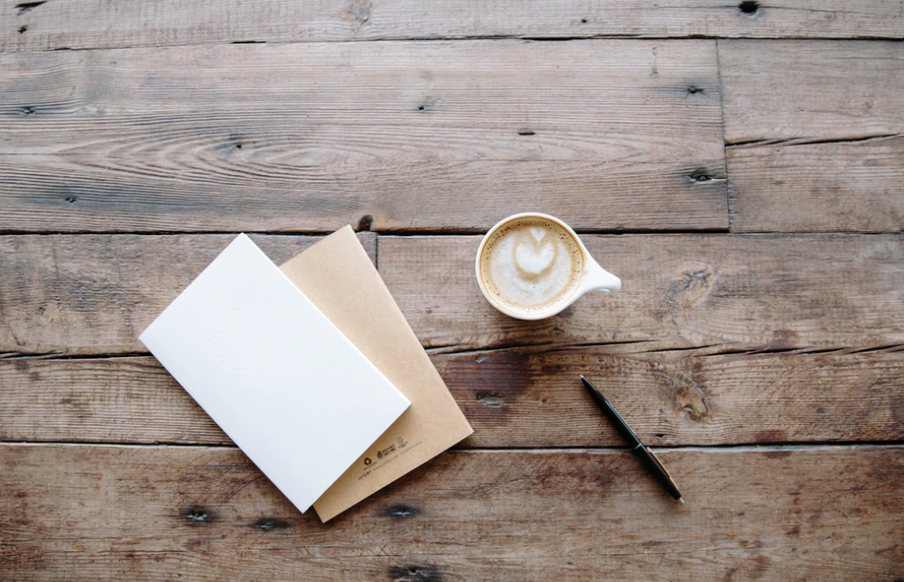 Paper, pen, and coffee sitting on a wooden table surface as a way to try offline marketing. If you want to learn how to build brand awareness for your blog, then keep reading.