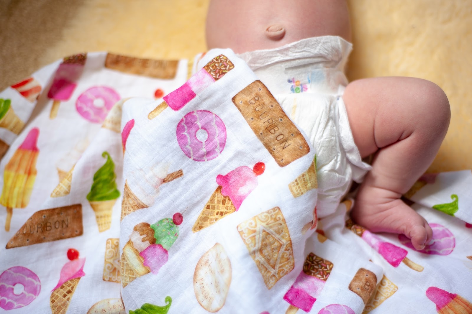 This image shows the lower half of a baby wearing only a diaper, slightly covered by a baby blanket.