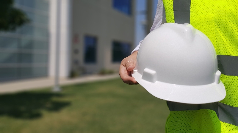 A worker in a hi-ves vest holds a hard hat by his hip