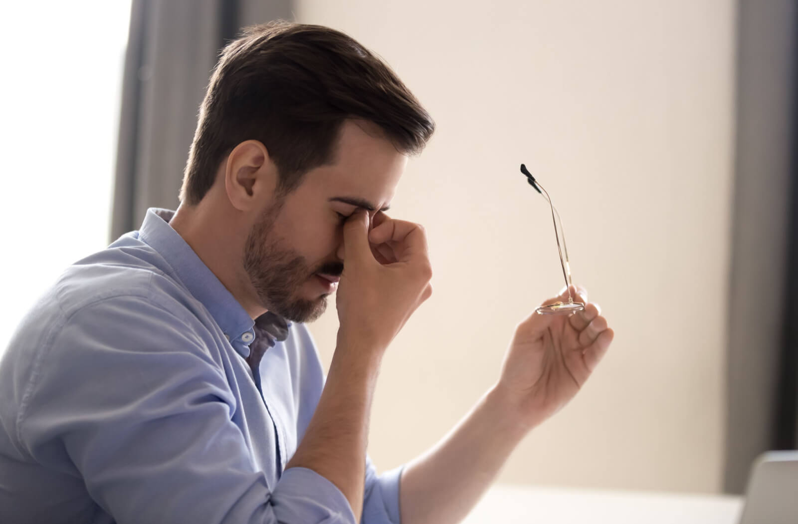 A man feels eyestrain on eye glasses he bought online. He took off his eyeglasses, holding spectacles in his hands massaging his eyes, having blurry vision or sight problems.