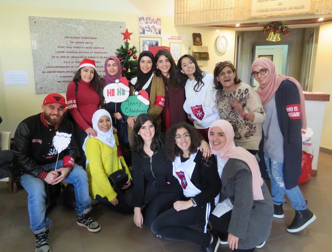 Above, volunteer youth from the Order of Malta Lebanon, a Catholic organization, and “Who Is Hussain?” a Shiite Muslim organization, gather at the order’s community health center in the Ain El Remmaneh suburb of Beirut Dec. 9 before heading out to decorate the homes of poor elderly Christians for Christmas. Below, volunteers pose with Gabriel and his sons, whom they visited Dec. 9 to decorate their Christmas tree.