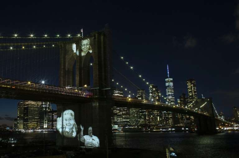 a bridge over a body of water: Black and white photos of Covid-19 victims are projected on to the Brooklyn Bridge as New York City marks more than 30,000 dead since the pandemic began