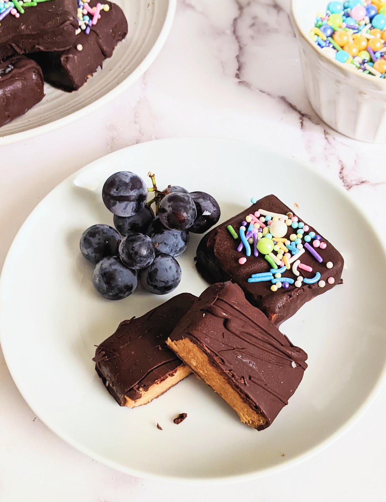 close up of peanut butter squares with a side of fruit on a plate