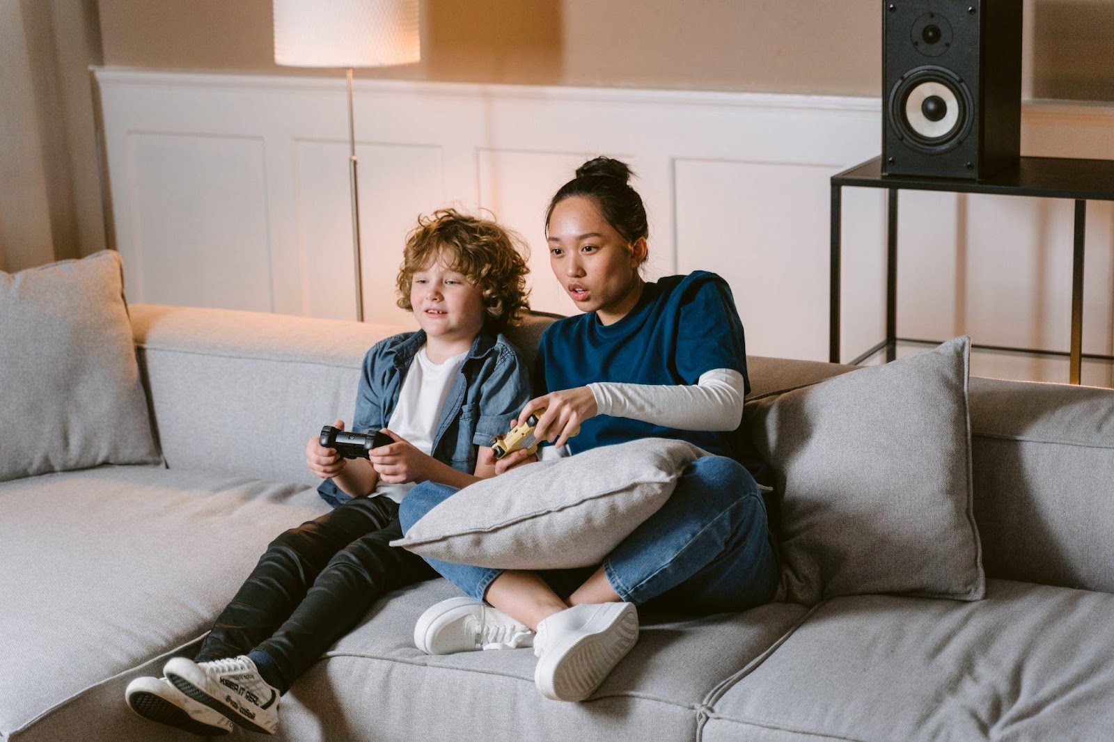 A woman and a guy playing video games while on the couch 
