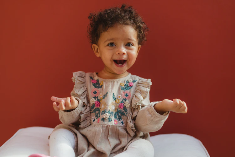 Smiling toddler with arms bent at the elbow and palms up.