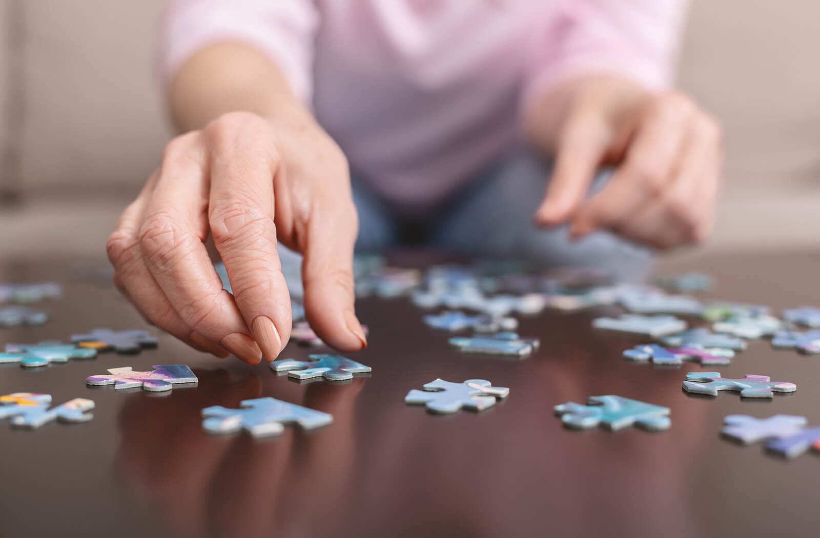 a close up of a woman's hands and puzzle pieces on a table. she is reaching for a puzzle piece