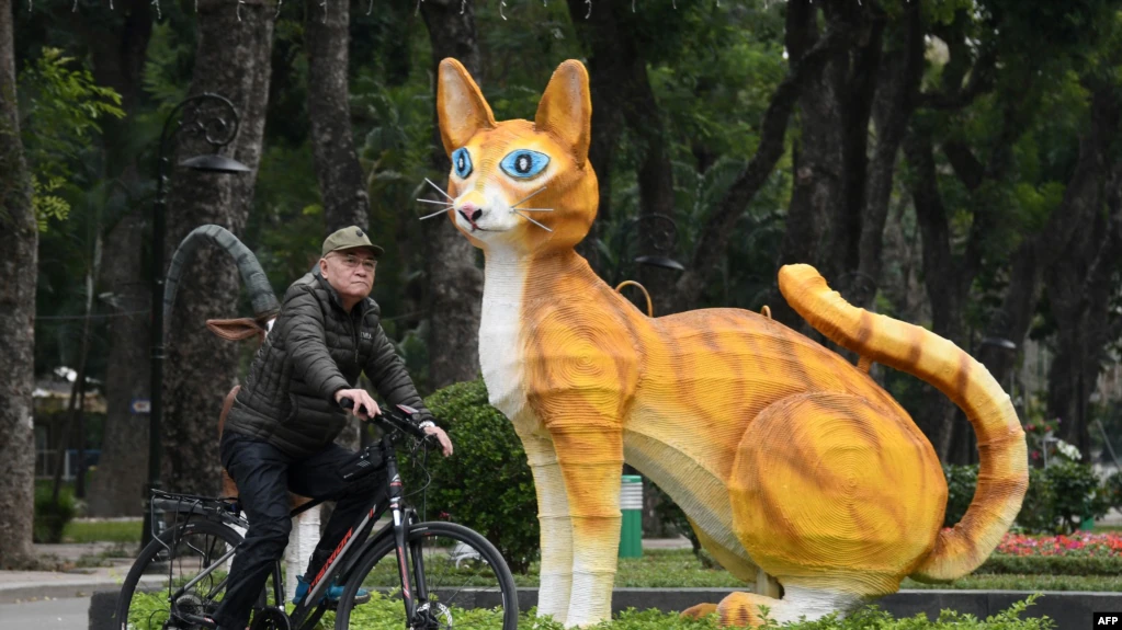 A man rides a bicycle past a cat statue at Thong Nhat Park in Hanoi