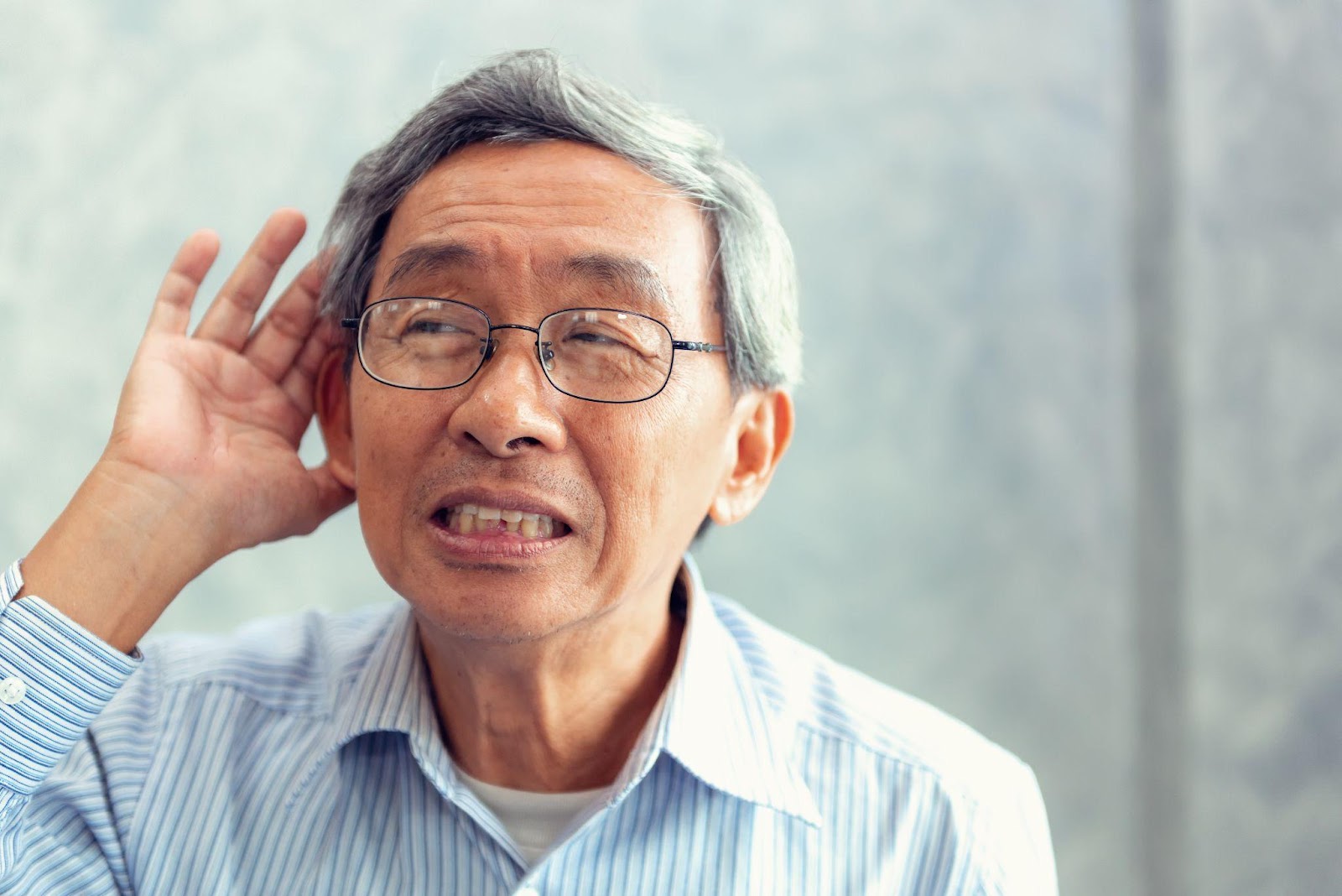 Elderly facing hearing loss cupping his ears trying to head sounds