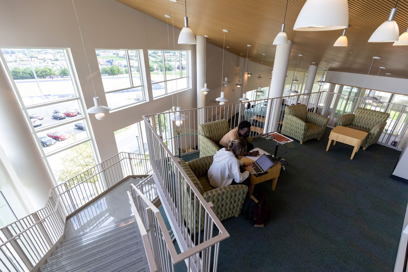 Two students sitting in a balcony lounge overlooking the Rose Library flex space with large windows.