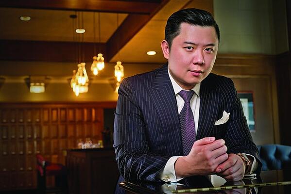 Dan Lok, emprendedor y experto en ventas está vestido de traje y corbata mira a la cámara.