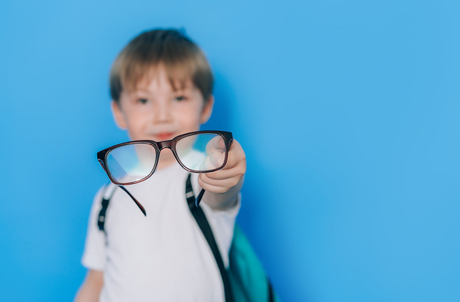 A boy holding a pair of prescription glasses out in front of him