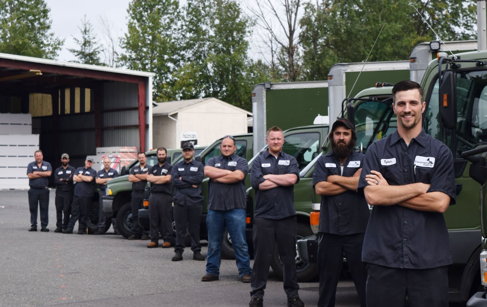 The Equipment Experts, Inc. team in a diagonal line, each person standing with arms folded against a different truck