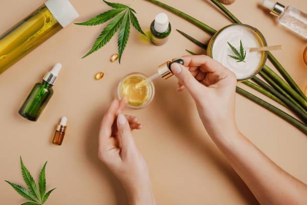 Pipette with CBD cosmetic oil in female hands on a table background with cosmetics, cream with cannabis and hemp leaves, marijuana Pipette with CBD cosmetic oil in female hands on a table background with cosmetics, cream with cannabis and hemp leaves, marijuana. Flat lay, top view. cbd products stock pictures, royalty-free photos & images