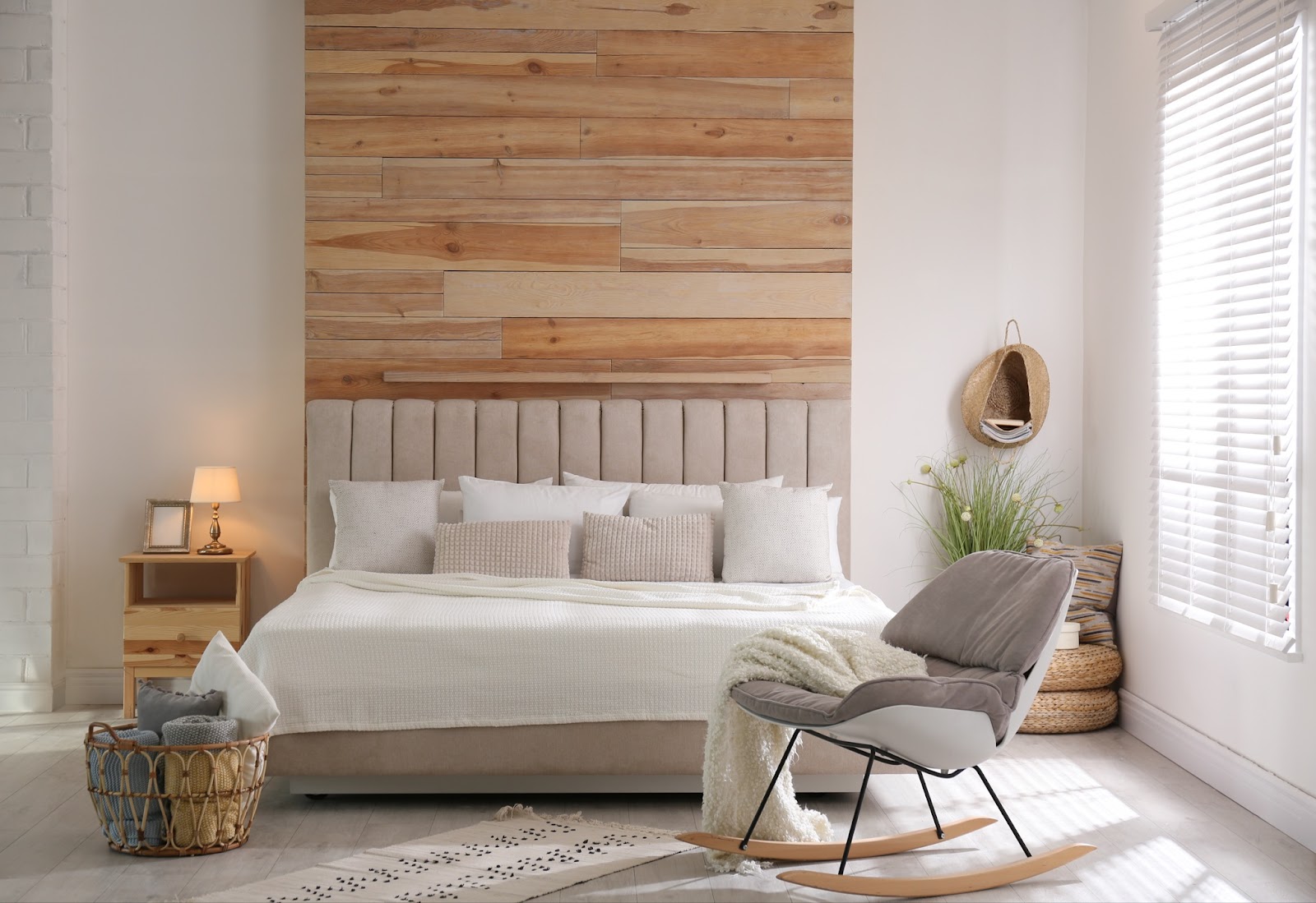 Scandinavian design master bedroom with neutral palette, a floor to ceiling wood panel centers the headboard on the wall and a modern rocker.  Multi-layered textures achieved through wicker, rattan, wood and textiles and plant life completes the modern design.