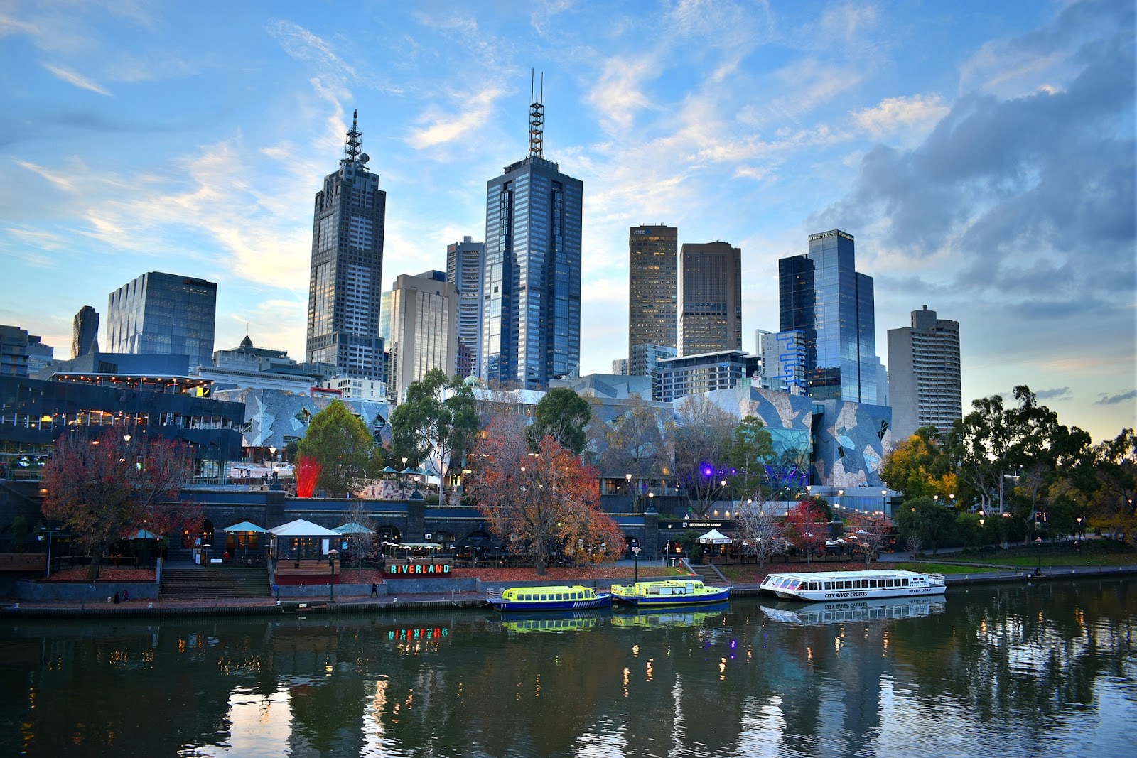 melbourne skyscrapers modern architecture and trees seen from across river with three parked boats during sunset