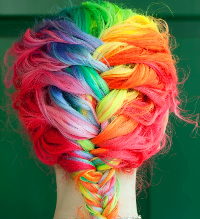 bunte Haare flechten - Regenbogen-Haare mit Fischgrätenzopf, lässige leicht gewellte Haare, Haare mit dunklem Ansatz und farbigen Strähnen, Mädchen mit dünnem Hals und weißer Haut, das vor einer grünen Wand steht