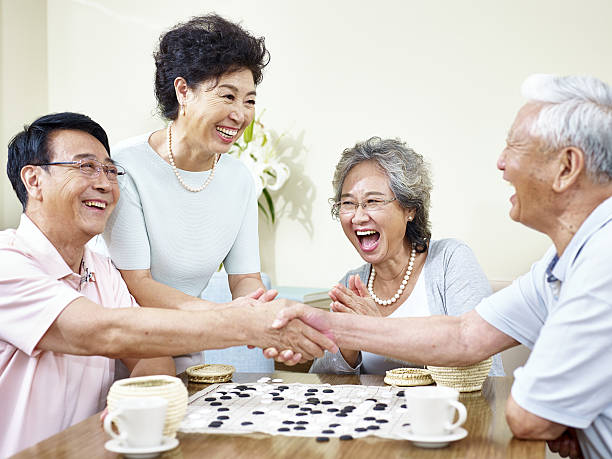 A group of senior citizens happily playing weiqi or go game, two elderly men having a handshake after the go game - How to Play Go Game or Weiqi for Beginners - The Gamerian Gaming Blog