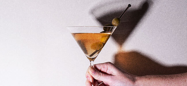 Hand holding a martini glass that is casting a shadow on the wall behind it.
