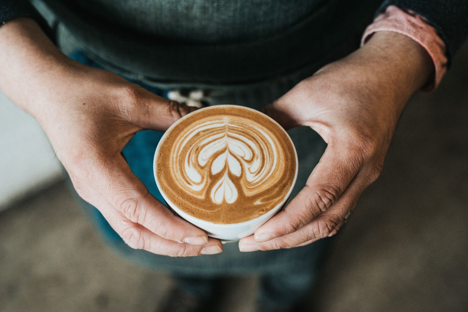 a top-down view of a man holding a cup of coffee with latte art of a flower at Bliss Bakery, one of Kelowna's best coffee shops.