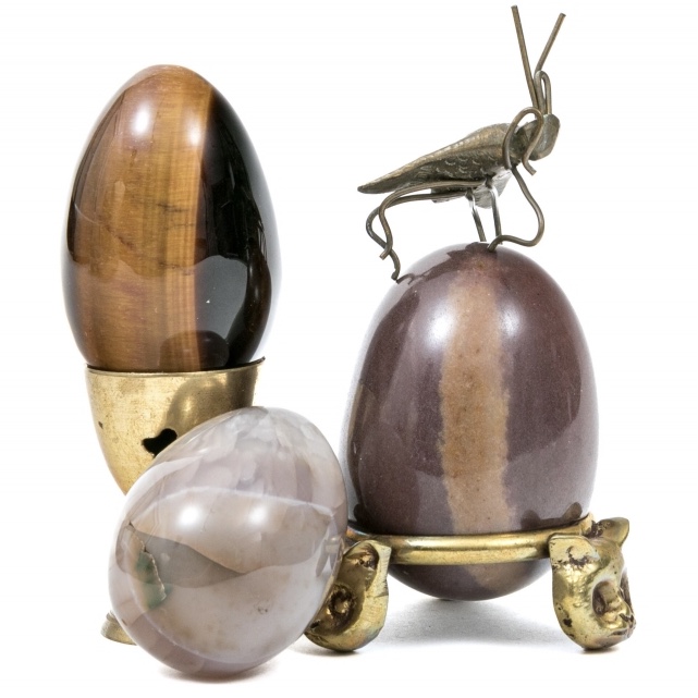Three quartz stone eggs (1) is a tiger's eye stone egg, (2) a light grey agate (3) is a purple-brown chalcedony with a brown band running through all displayed on metallic stands from the Dr. Paul Zahl estate collection