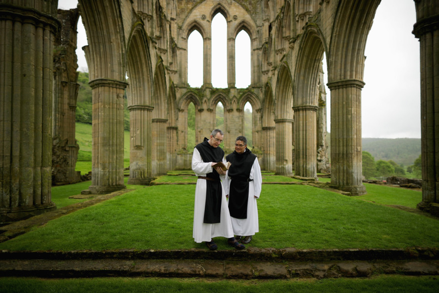 THIRSK, ENGLAND - MAY 26:    Cistercian Monks, Father Joseph and Brother Bernard John (R) read from a 500-year-old prayer book as they visit the ruins of Rievaulx Abbey in North Yorkshire on May 26, 2016 in Thirsk, England. The monks were visiting the Abbey to view the new exhibition centre and museum at the English Heritage site, which tells the story of Rievaulx from its foundation in 1132 to its suppression by Henry VIII. Rievaulx Abbey was the first monastery of the reforming Cistercian order in the North of England.  At its peak in the 1160's it was home to a community of over 600 men, who passed their lives in an ordered daily sequence of religious services, reading and manual work.  (Photo by Christopher Furlong/Getty Images)