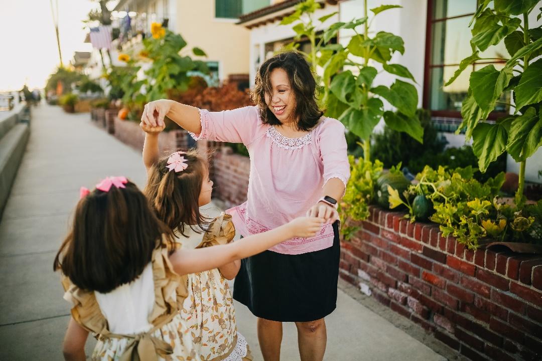 a woman holding the hands of two little girls on a sidewalk