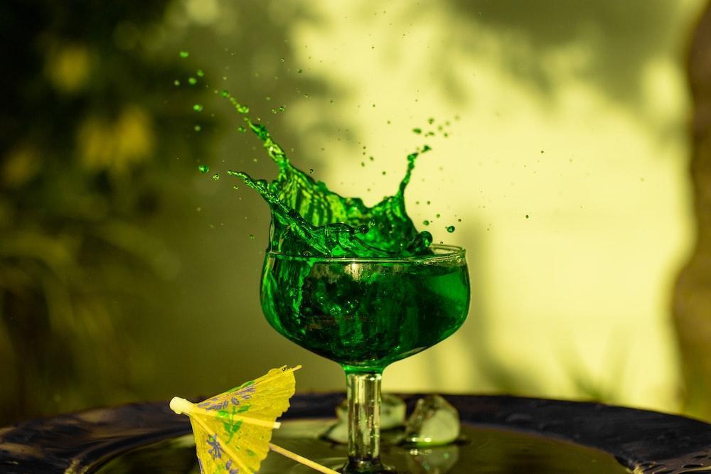 a green liquid splashing into a glass with an umbrella