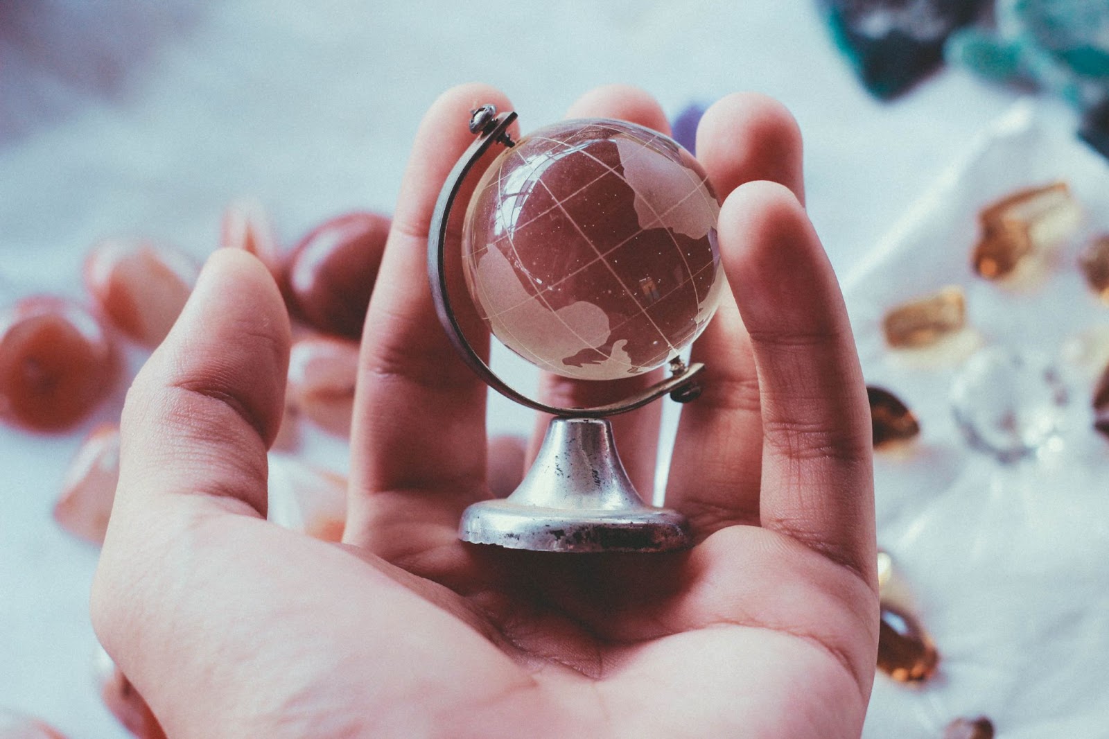 A white hand holding a miniature glass globe. 