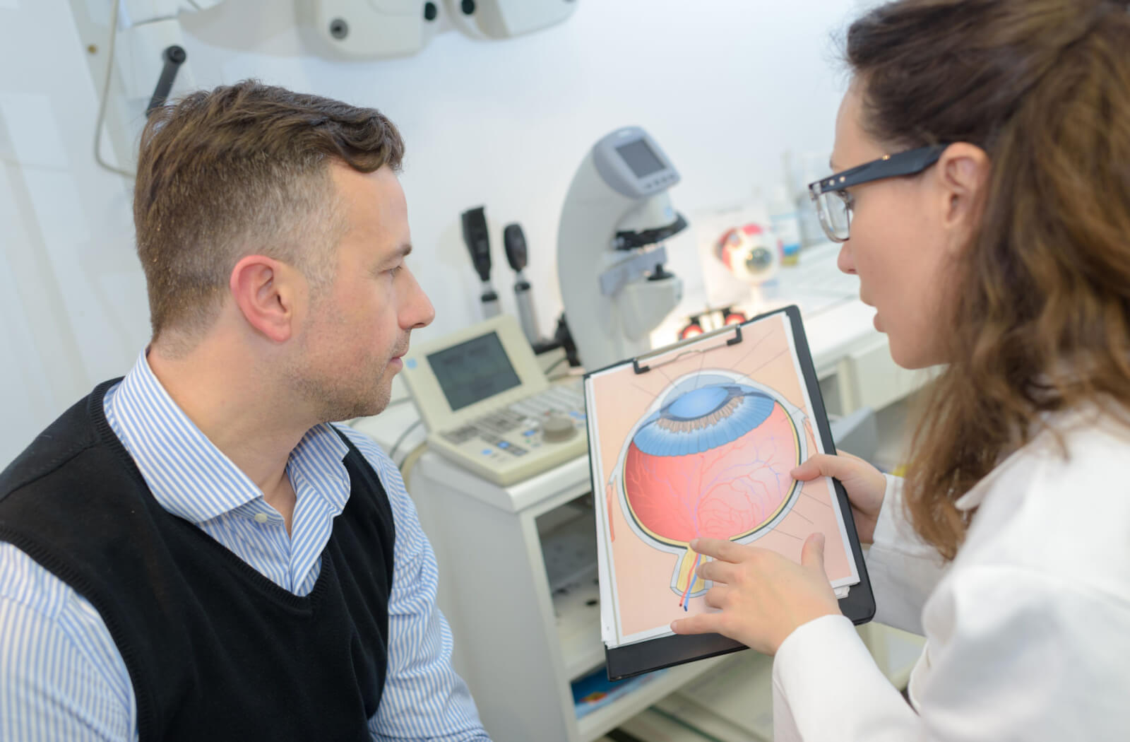 A patient sitting in an exam room looking at a diagram of an eye with his optometrist