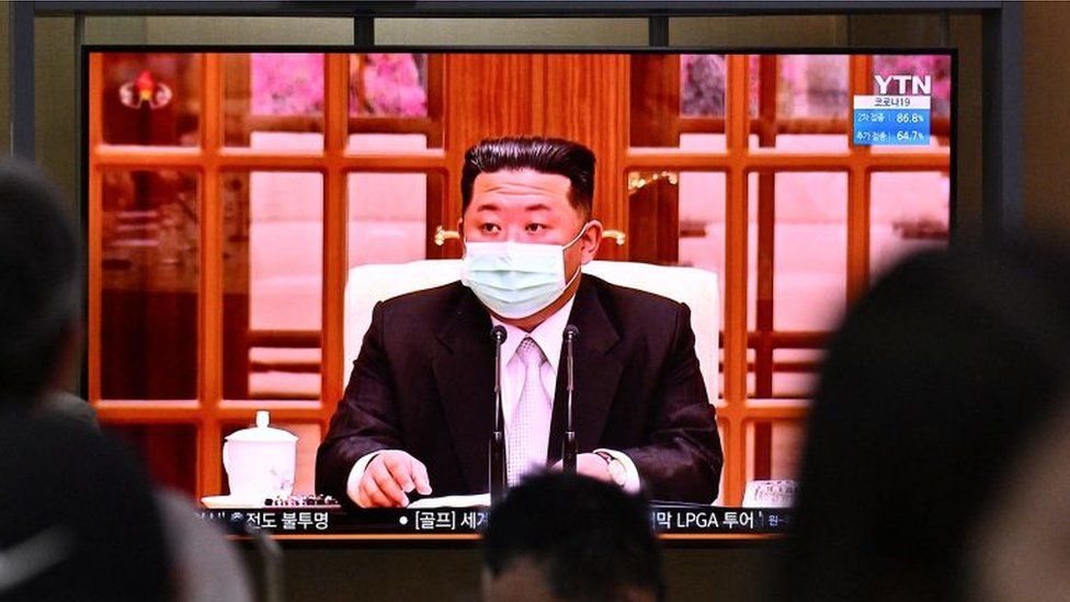 ผู้คนนั่งใกล้หน้าจอแสดงข่าวที่ออกอากาศที่สถานีรถไฟในกรุงโซลเมื่อวันที่ 12 พฤษภาคม พ.ศ. 2565 ของผู้นำเกาหลีเหนือ Kim Jong Un ที่ปรากฏตัวในหน้ากากทางโทรทัศน์เป็นครั้งแรกเพื่อสั่งปิดประเทศหลังจากที่เกาหลีเหนือยืนยันครั้งแรก เคยมีกรณี Covid-19