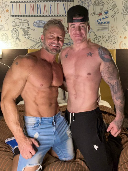 Greg Dixxon posing in jeans on the bed with adult gay onlyfans creator JJ Knight
