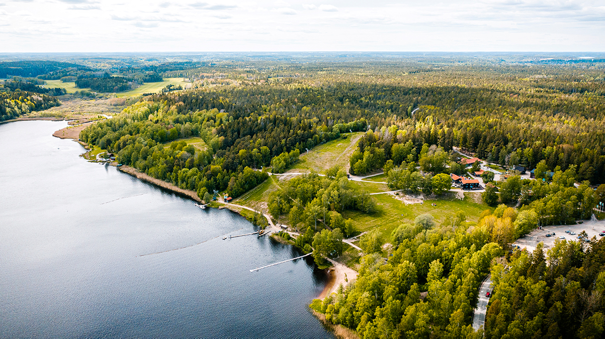 Drönarbild på Lida Friluftsgård med gröna träd och sol.