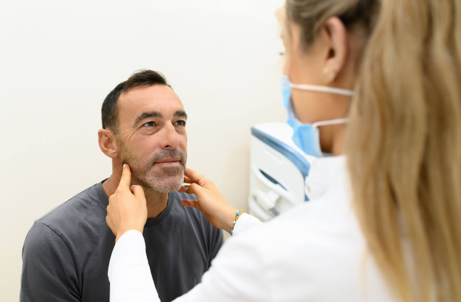 A female aesthetician with a mask on analyzing a man in a clinic.
