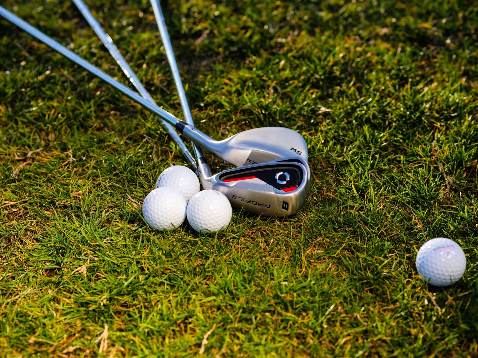 Clubs laying grass beside golf balls 