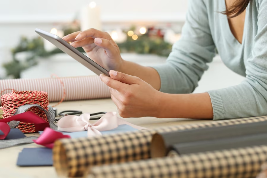 A hand using a tablet on a table, surrounded by scattered fabrics