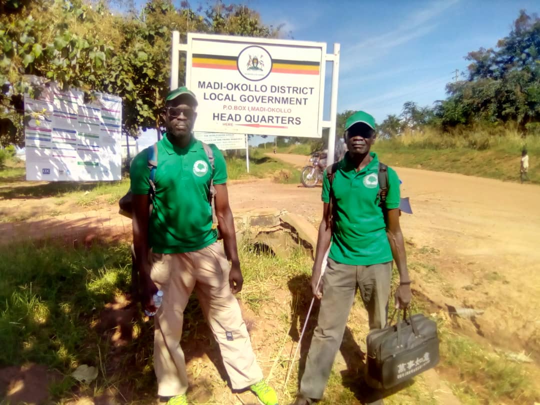 Two men stand beside a dirt road in front of a local government HQ sign