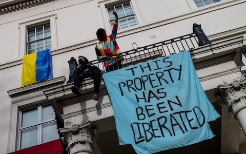 Protesters hand a banner from the front of the Belgravia mansion