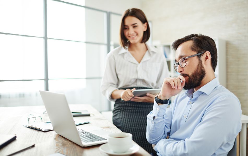 A man and a woman in an office environment looking at a laptop.