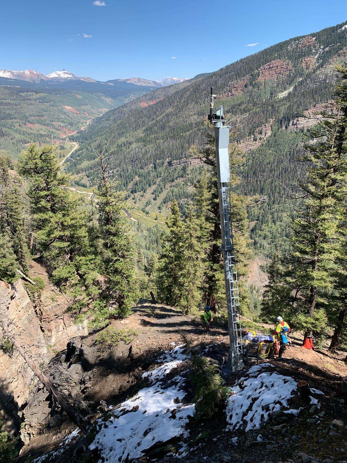 In slightly snowy mountains, a crew is installing one of five towers above CO 145 in southwest Colorado