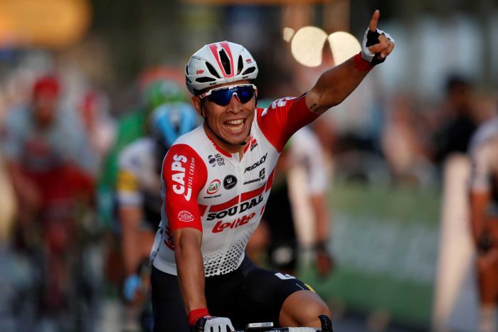 A smiling Caleb Ewan raises one finger after crossing the finish line.