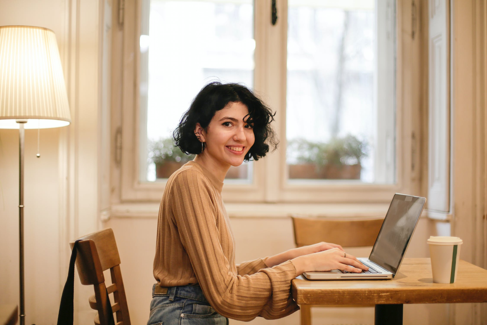 Woman working on her laptop at a desk while smiling towards the camera