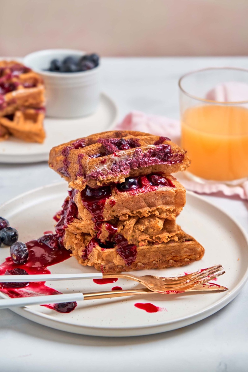 a plate of vegan waffles topped with blueberry sauce served with a cup of juice
