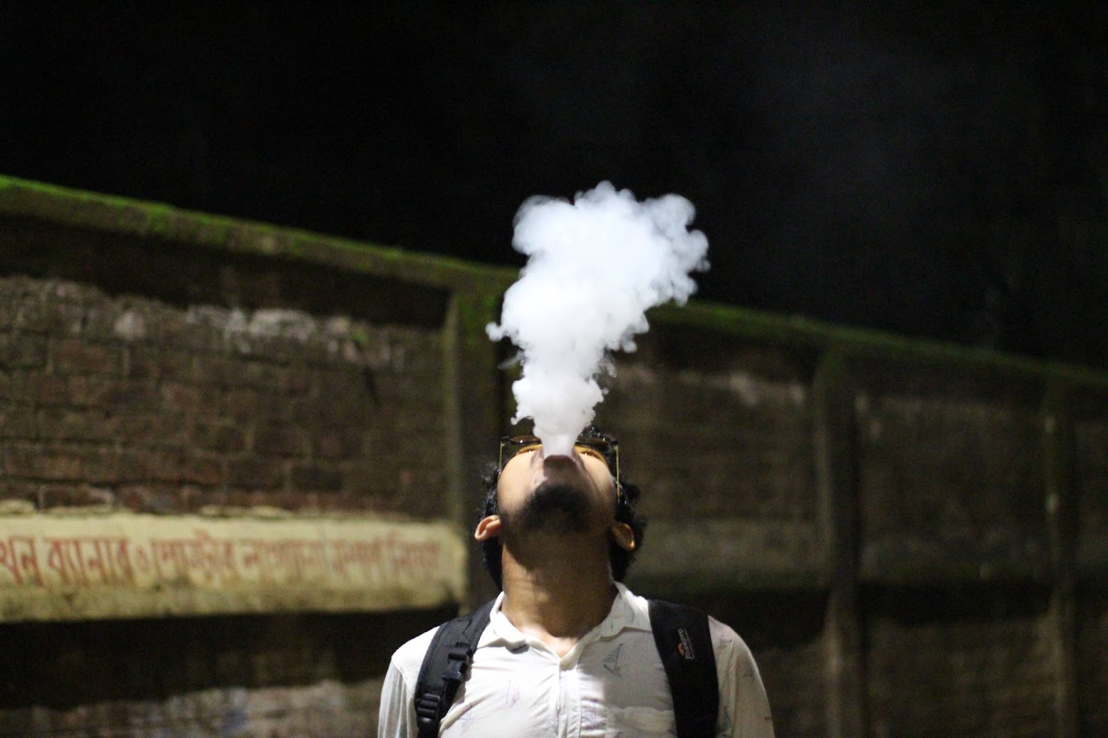 A man looking up exhaling a large vape cloud