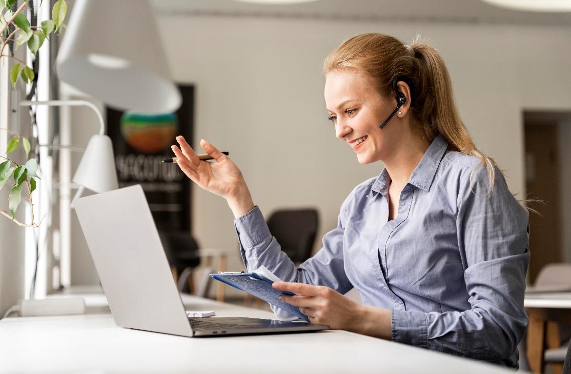 Picture of a woman working at a desk on a laptop wearing headsets
